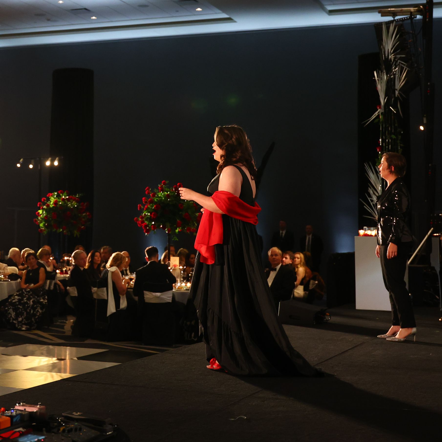 Two women in fancy attire singing on a stage
